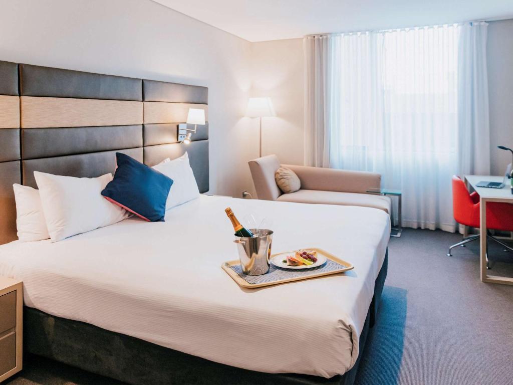 a hotel room with a bed with a tray of food at Novotel Newcastle Beach in Newcastle