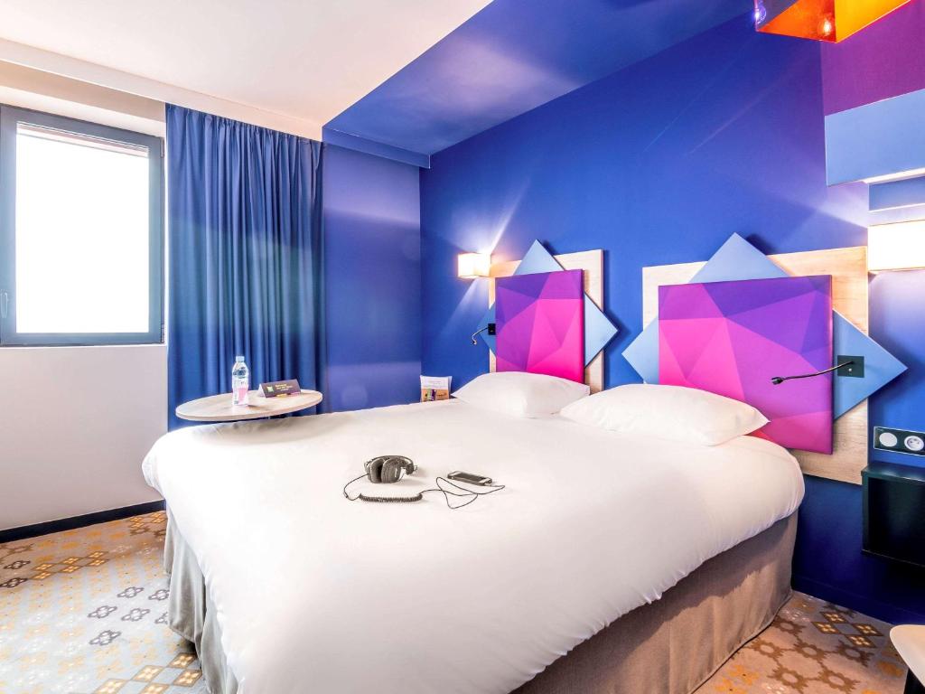 - une chambre avec un grand lit blanc aux murs violets dans l'établissement ibis styles Albi Centre Le Theatro, à Albi