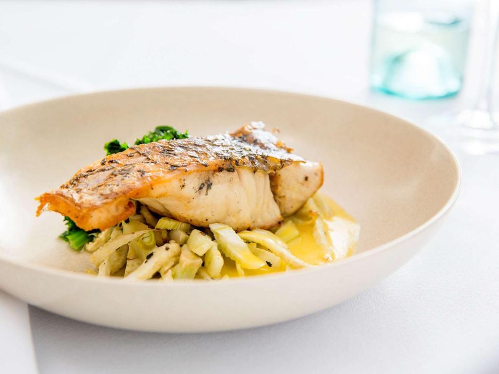 a white bowl of food with fish and pasta at Novotel Newcastle Beach in Newcastle
