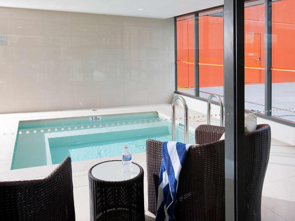 a swimming pool with two chairs and a table at Novotel Newcastle Beach in Newcastle