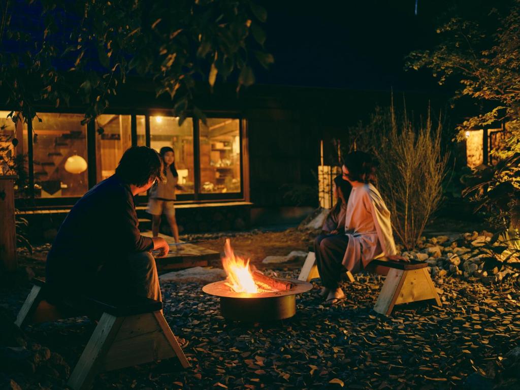 two people sitting around a fire pit at night at 古民家宿るうふ 澤之家 in Fuefuki