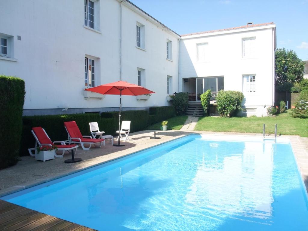 a patio area with a pool, chairs, and a blue umbrella at Hôtel des Biches in Nuaillé