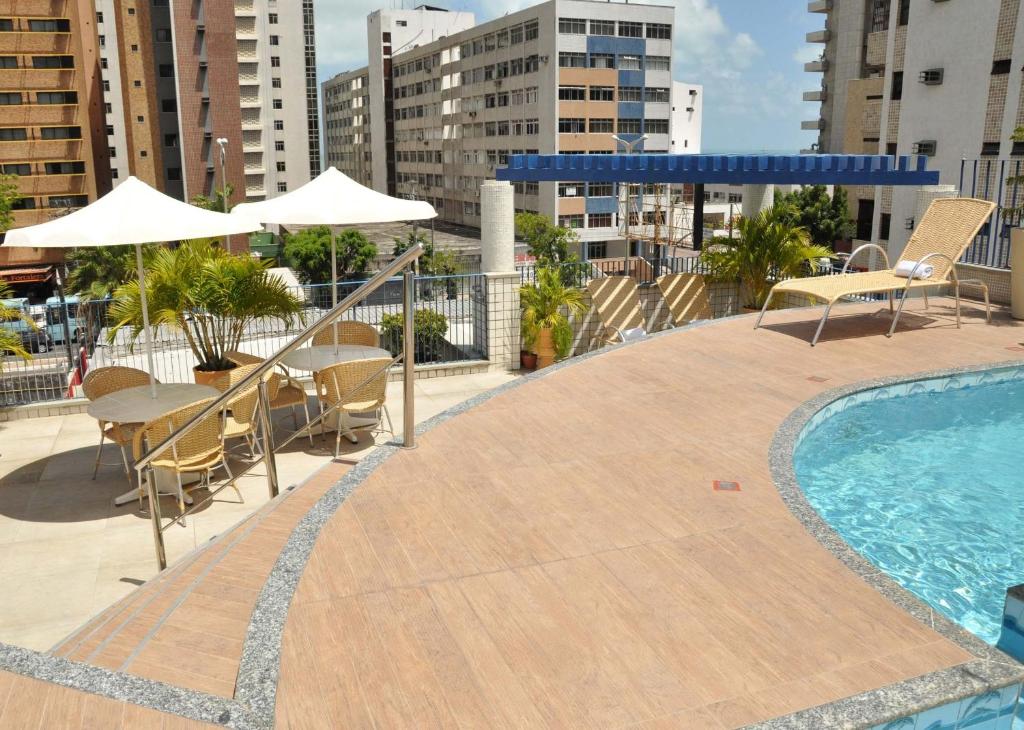 una piscina con sillas, mesas y sombrillas en un edificio en Vila Azul Praia Hotel, en Fortaleza