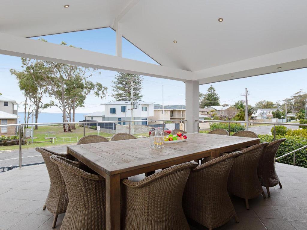 a wooden table with chairs on a patio at Beauty and the Beach', 88 Foreshore Drive - large home with WIFI & water views in Salamander Bay