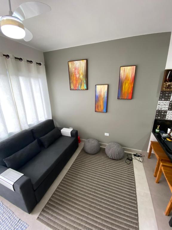 uma sala de estar com um sofá preto e pinturas na parede em Apto Novo Duplex em Juqhey em Juqueí