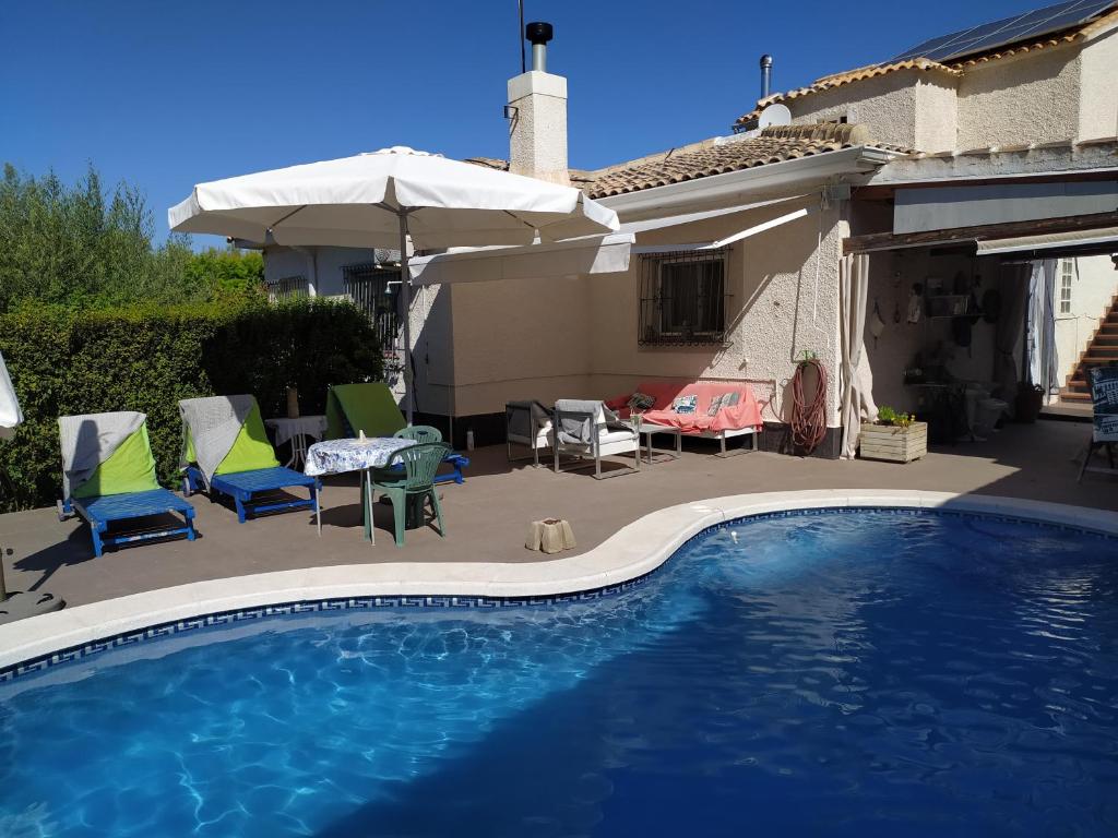 a swimming pool with chairs and umbrellas next to a house at Bonita habitación independiente in Orihuela Costa