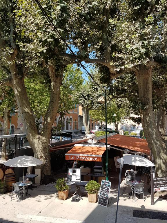 a cafe with tables and umbrellas on a city street at Hôtel de Provence in Brignoles