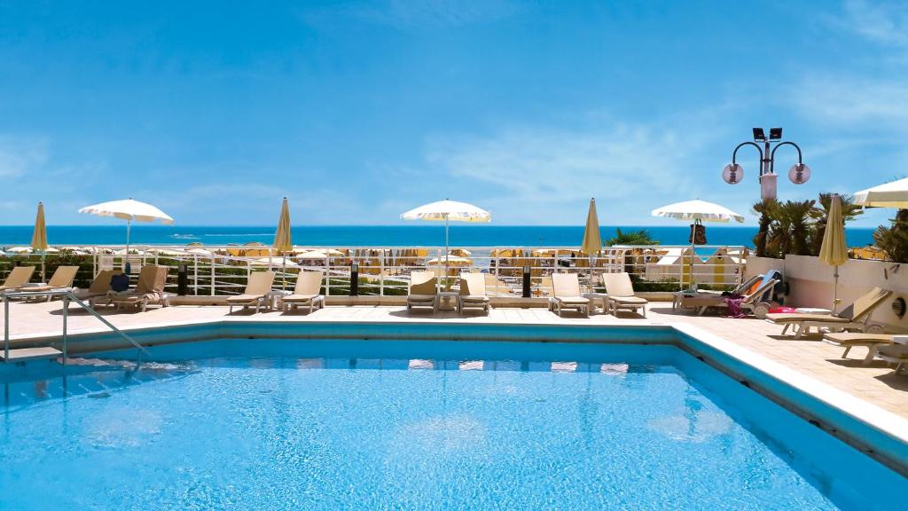 uma piscina com cadeiras e guarda-sóis e o oceano em Hotel Bristol em Lido di Jesolo