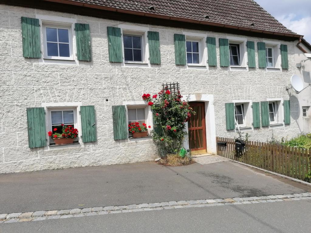 Casa de ladrillo blanco con flores y ventanas con contraventanas verdes en Ferienhaus Wastl 91355 Hiltpoltstein,Möchs 11, en Hiltpoltstein
