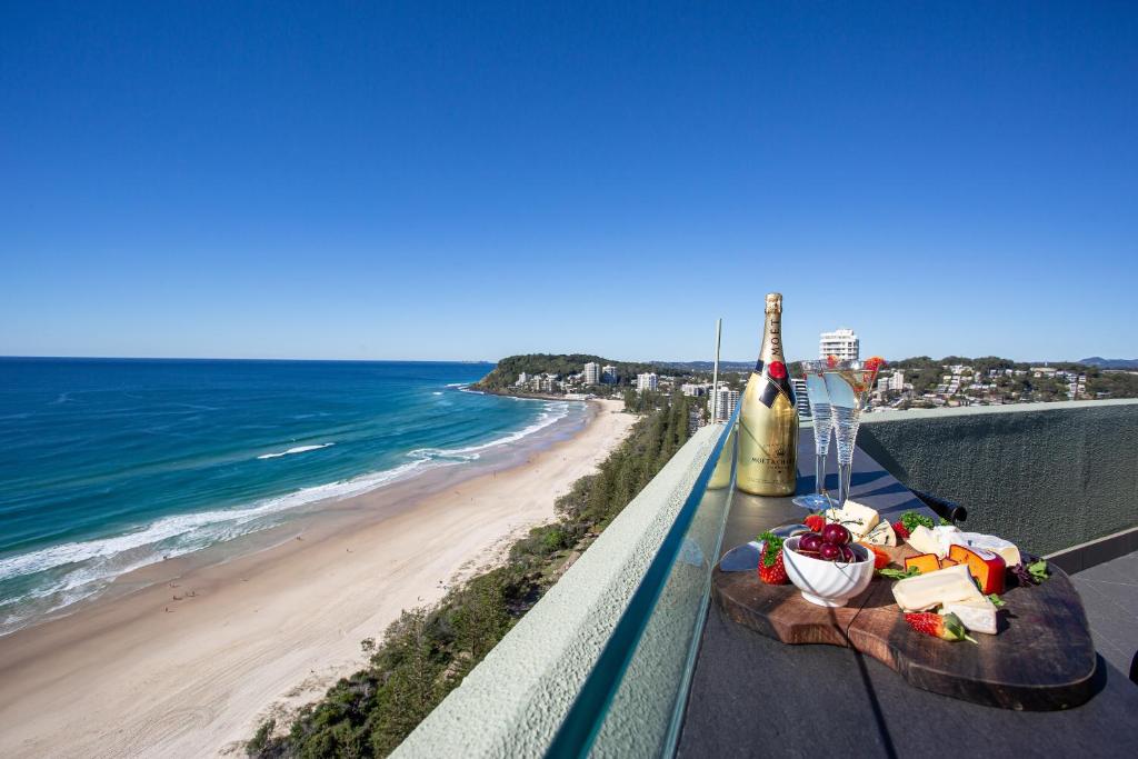a table with food and a bottle of wine and the beach at Burleigh Esplanade Apartments in Gold Coast