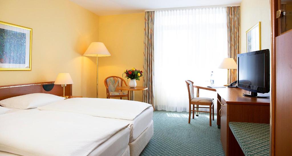 Habitación de hotel con cama, escritorio y TV. en Victor's Residenz-Hotel Gera, en Gera