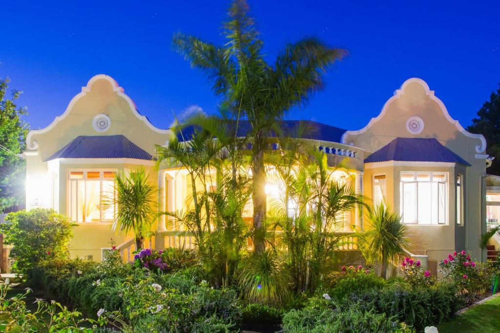 een groot wit huis met palmbomen ervoor bij 6 on Kloof Guest House in Bredasdorp