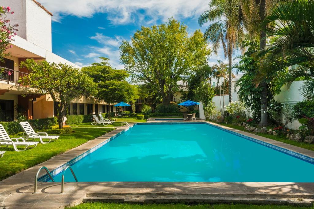 una piscina en un patio con sillas y árboles en Hotel Puerta Del Sol Guadalajara, en Guadalajara