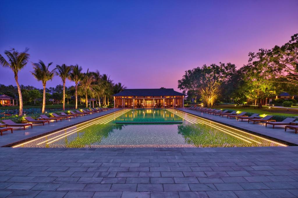 a swimming pool with chairs and a building at night at Azerai Can Tho in Can Tho