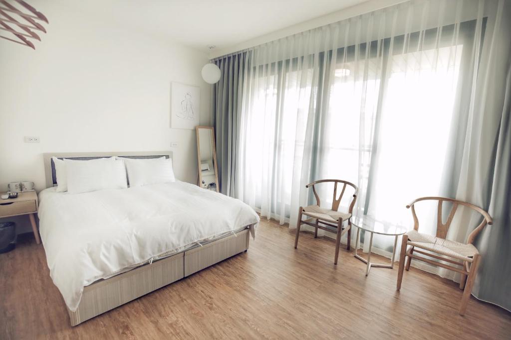 um quarto com uma grande cama branca e 2 cadeiras em 66 south em Tainan