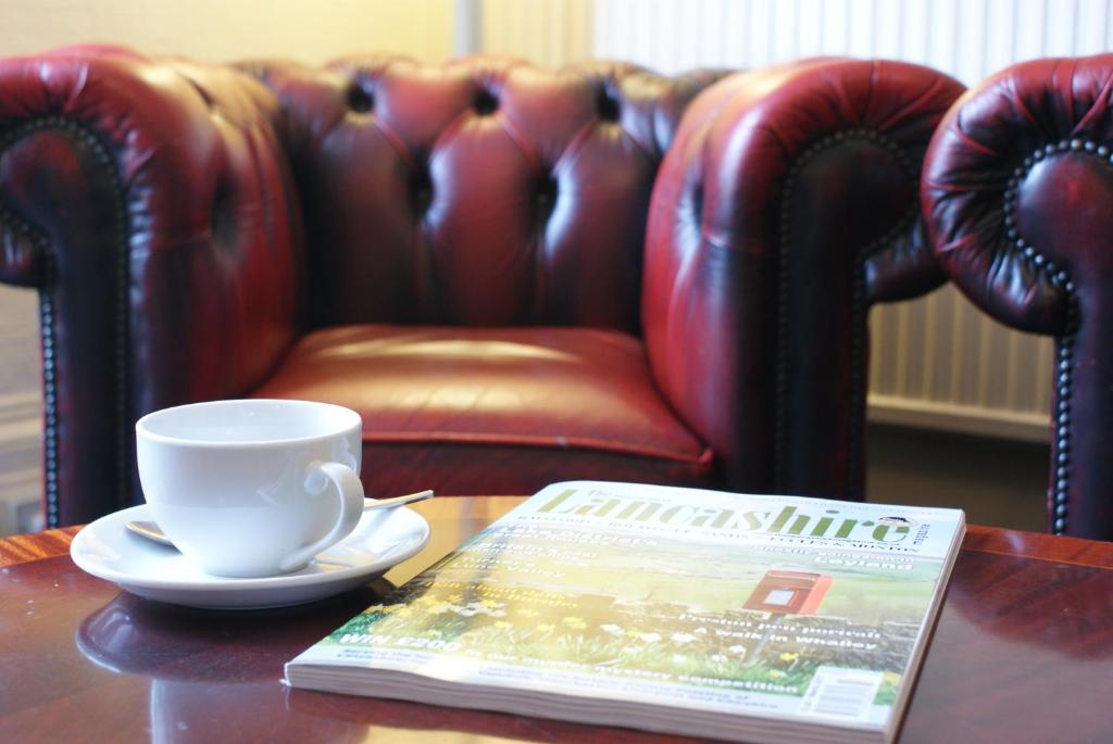 a coffee cup and a book on a table with a coffee cup and a newspaper at Adelphi Guest House in Southport