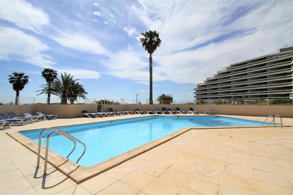 einen Pool mit Stühlen und einer Palme in der Unterkunft COPACABANA - 3 pièces vue mer avec piscine et parking in Canet-en-Roussillon