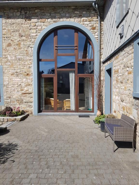 un edificio de piedra con una gran ventana y un banco en La Source d'Arimont en Malmedy