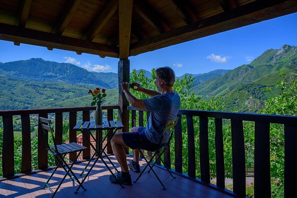 a woman sitting on a chair on a porch with a view of mountains at La Xamoca Apartamentos Rurales in Campiellos
