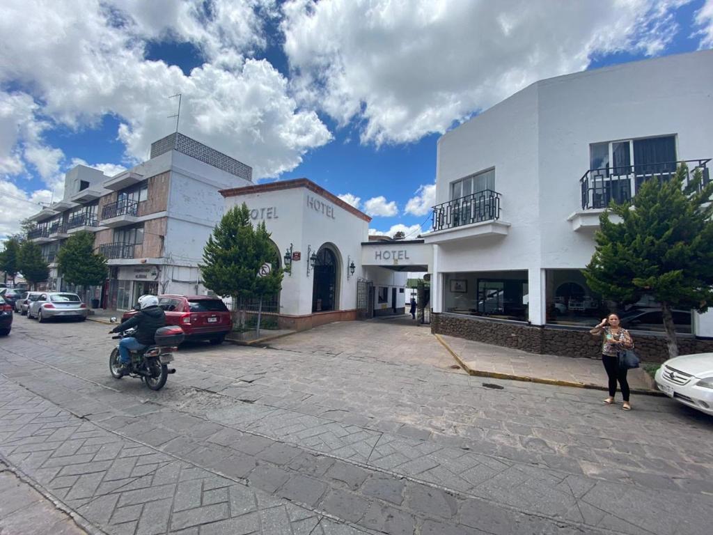 Ein Mann, der mit dem Motorrad eine Straße entlang fährt, neben einem Gebäude in der Unterkunft Hotel Zacatecas Courts in Zacatecas