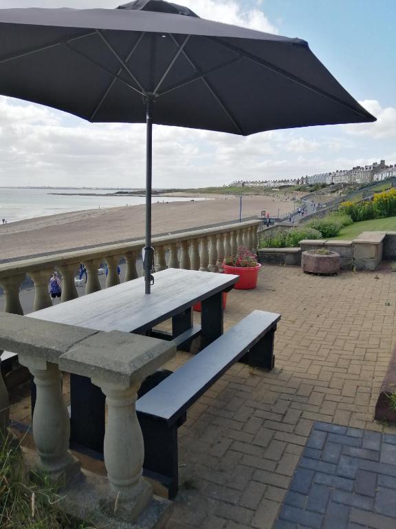 a picnic table with an umbrella on the beach at Captains Lodge in Newbiggin-by-the-Sea