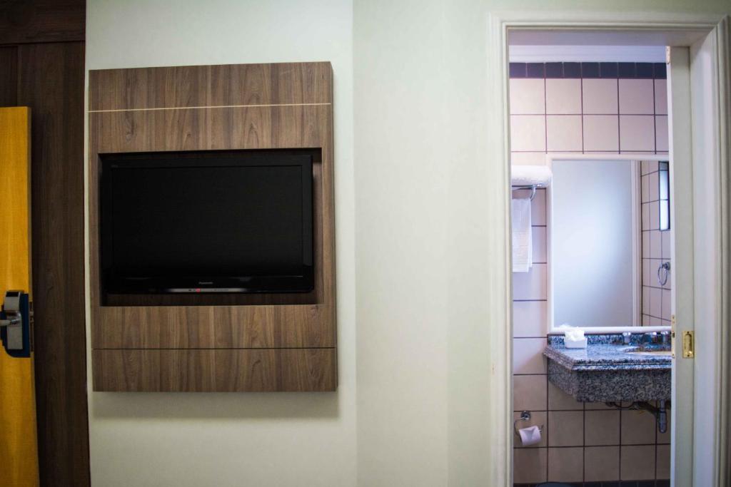 TV de pantalla plana en una pared junto a un baño en Caitá Hotéis, en Concórdia