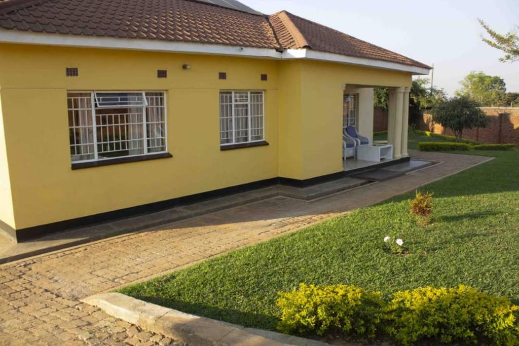 ein gelbes Haus mit Rasen davor in der Unterkunft Chrinas Guest House in Lilongwe