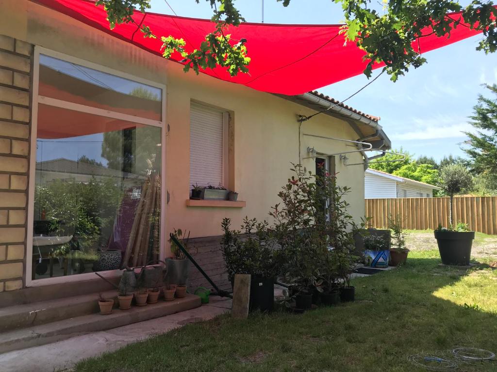 una casa con una sombrilla roja en el patio en le petit jour classé 3 étoiles Maison 6 pers climatisée - Audenge - Bassin d'Arcachon en Audenge