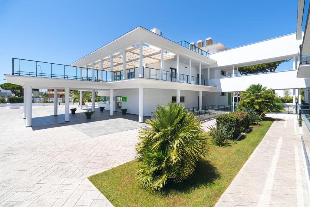 a large white building with palm trees in front of it at Complejo Al Sur in Chiclana de la Frontera