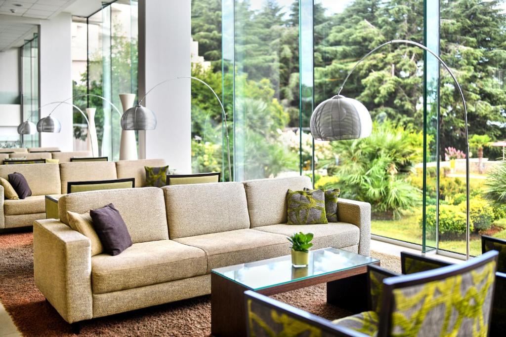 a living room with a couch and tables and windows at Hotel Mediteran Plava Laguna in Poreč