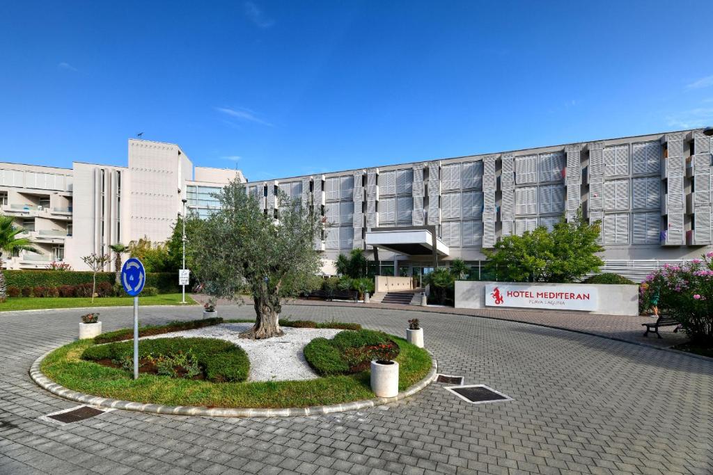 a building with a tree in the middle of a street at Hotel Mediteran Plava Laguna in Poreč