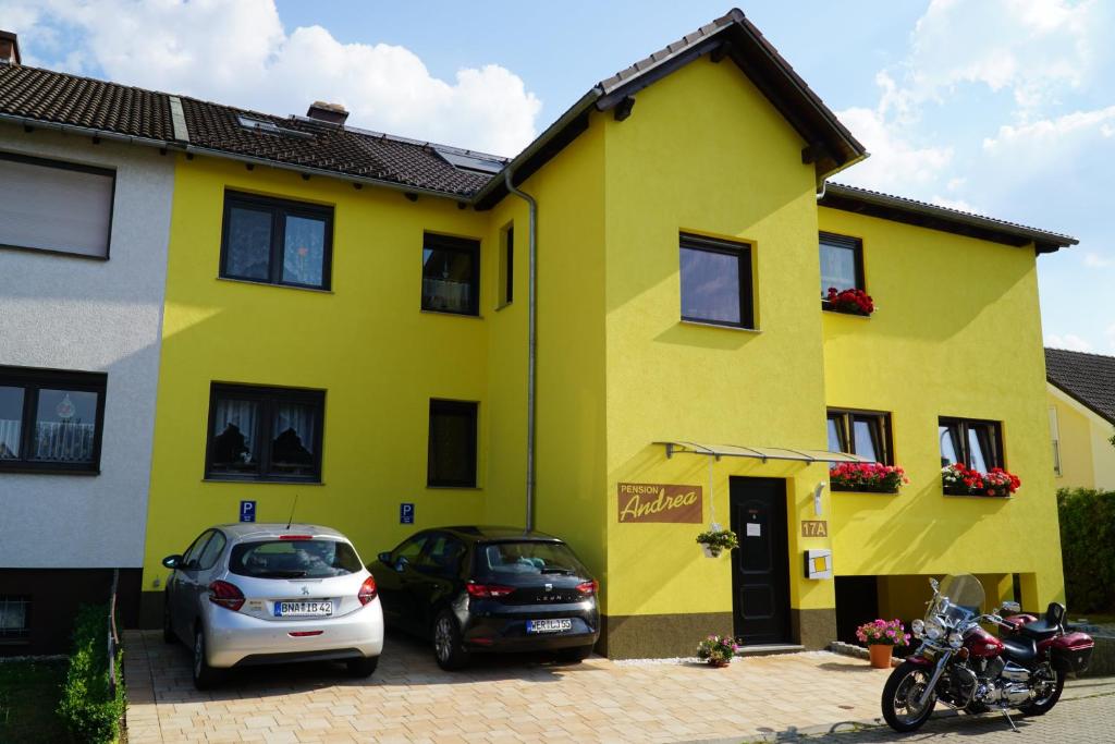 żółty dom z samochodami zaparkowanymi przed nim w obiekcie Pension Andrea w mieście Lugau