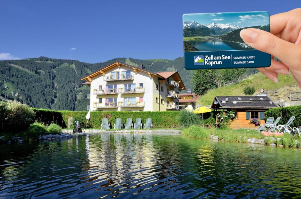 a person taking a picture of a house next to a lake at Berghotel Jaga-Alm in Zell am See