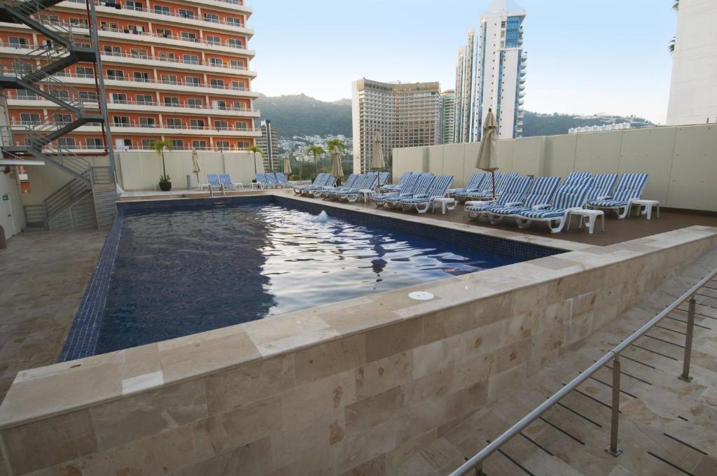 a swimming pool on the roof of a building with chairs at One Acapulco Costera in Acapulco