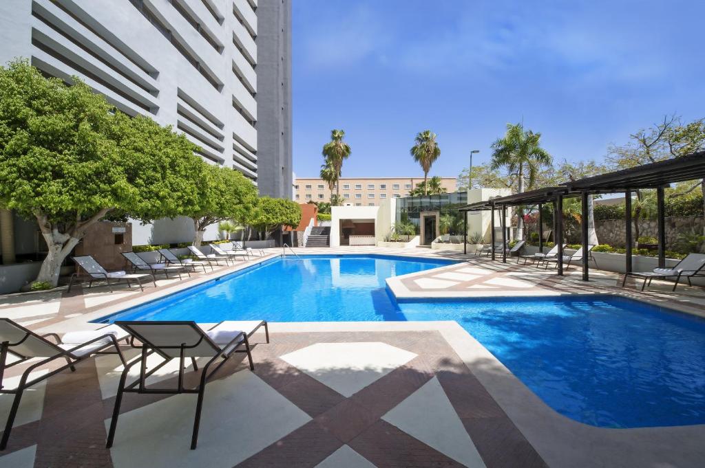 a swimming pool with chairs and a building at Fiesta Americana Hermosillo in Hermosillo