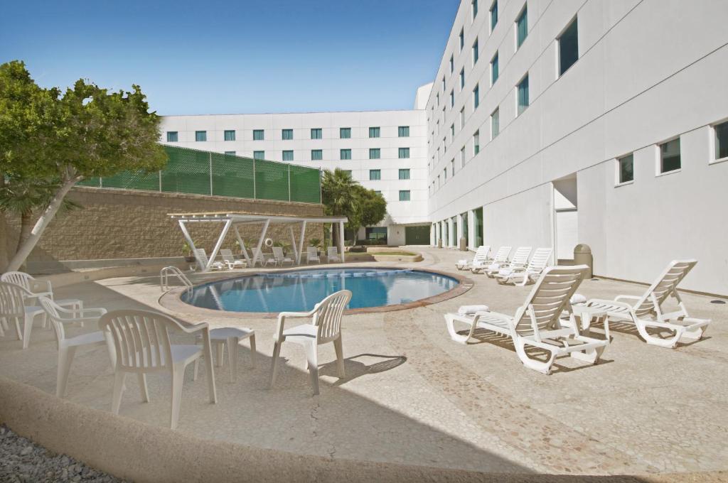 a patio with chairs and a pool and a building at Fiesta Inn Mexicali in Mexicali