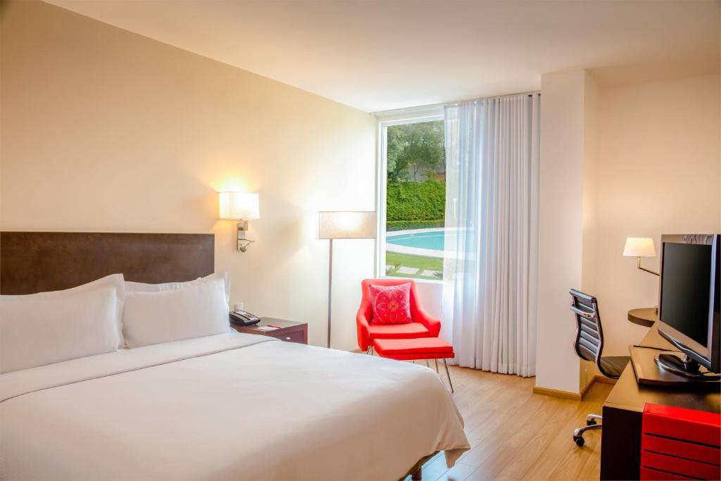 um quarto de hotel com uma cama e uma cadeira vermelha em Fiesta Inn Perinorte em Cidade do México
