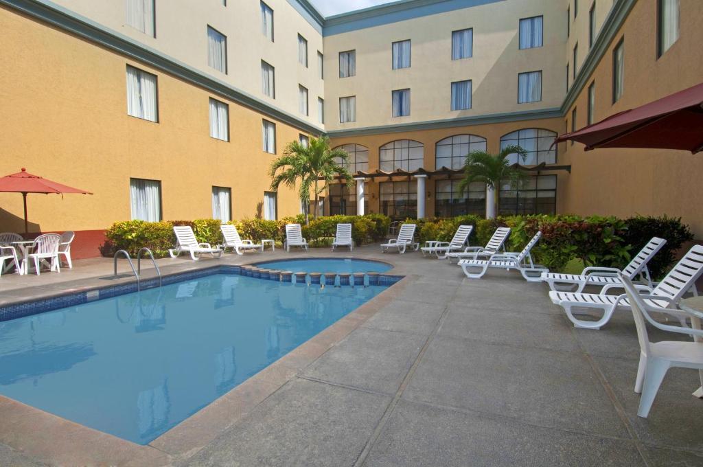 un hôtel avec une piscine, des chaises et un bâtiment dans l'établissement Fiesta Inn Poza Rica, à Poza Rica de Hidalgo