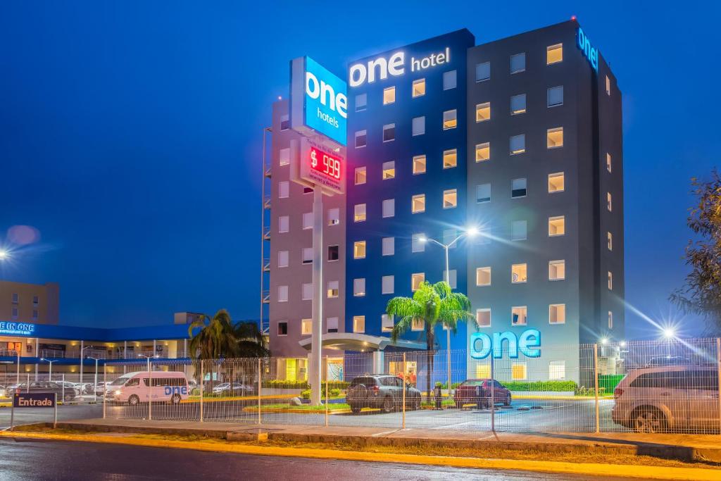 ein einziges Hotelgebäude mit Autos auf einem Parkplatz in der Unterkunft One Monterrey Aeropuerto in Monterrey