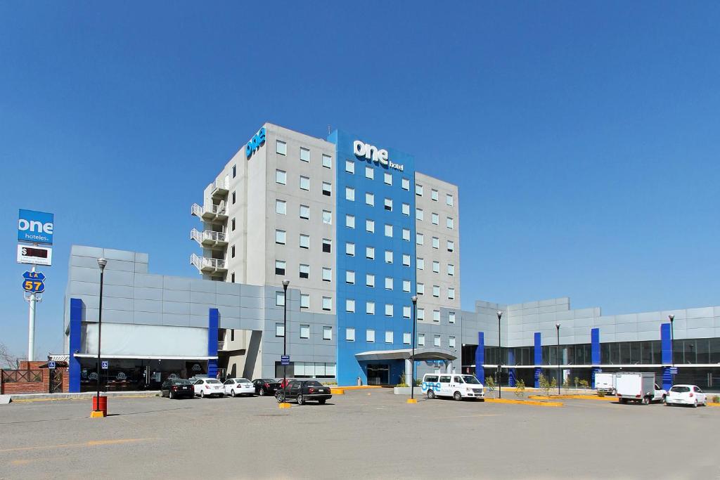 een groot gebouw met auto's geparkeerd op een parkeerplaats bij One Queretaro Aeropuerto in Querétaro