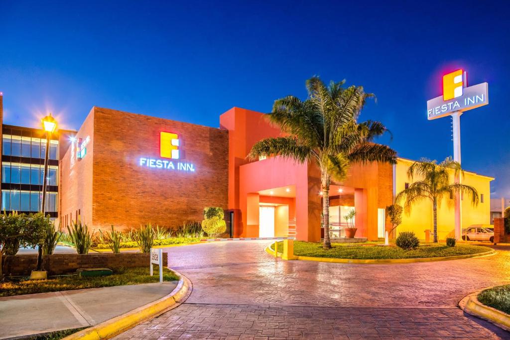 un hotel exterior por la noche con un letrero de la calle y palmeras en Fiesta Inn Monterrey la Fe, en Monterrey