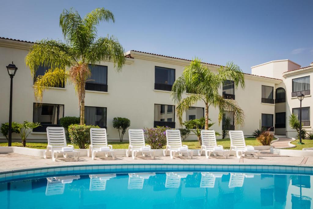 a pool with chairs and palm trees and a building at Fiesta Inn Monterrey la Fe in Monterrey