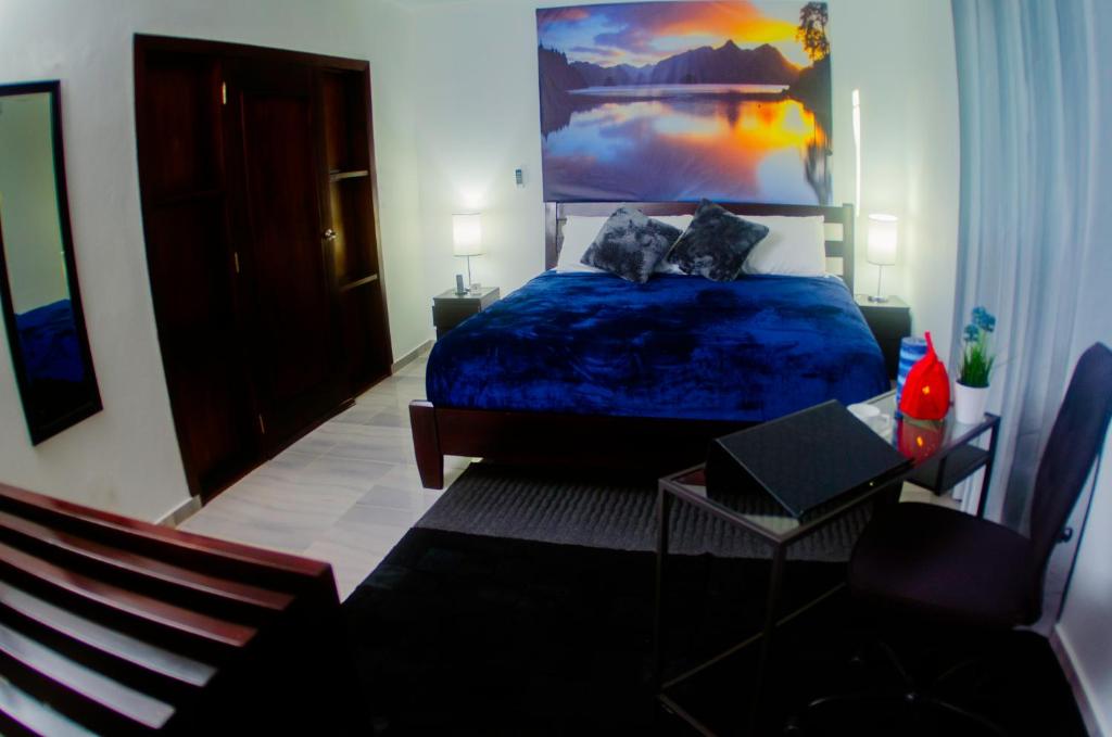 a bedroom with a blue bed with a large painting on the wall at Hotel Casa Jum in Santiago de los Caballeros