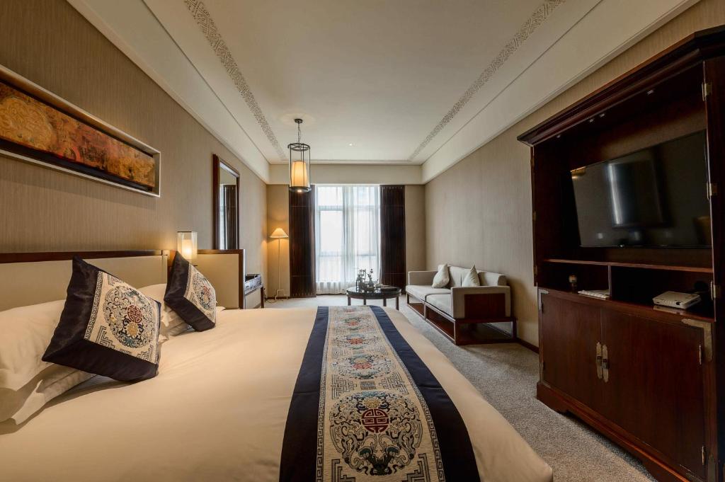 a hotel room with a large bed and a flat screen tv at Tongquetai Jinling Hotel Tongling Anhui in Tongling