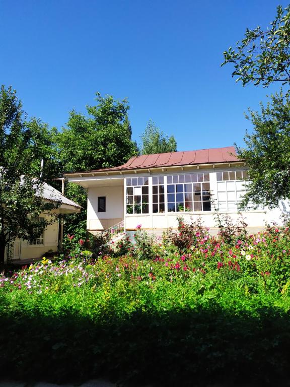 a white house with a lot of flowers in front of it at Riverside Guest house Mashkhur in Arslanbob