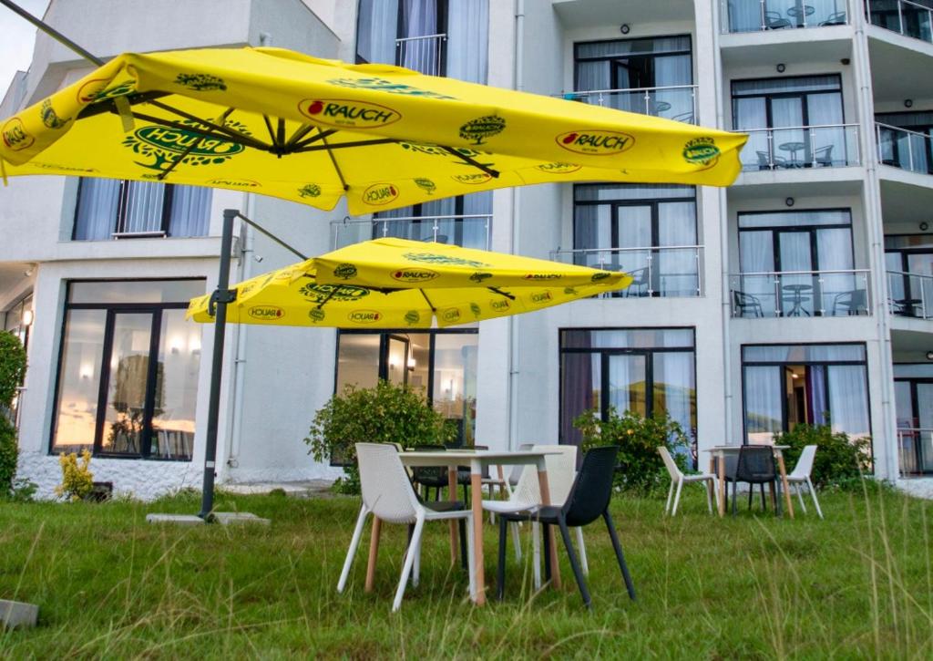 a table and chairs with yellow umbrellas in front of a building at Hotel Scala in Shekhvetili