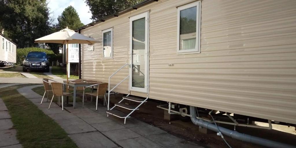 a table with chairs and an umbrella next to a house at Haven Rockley Park,Lytchett Bay View in Hamworthy