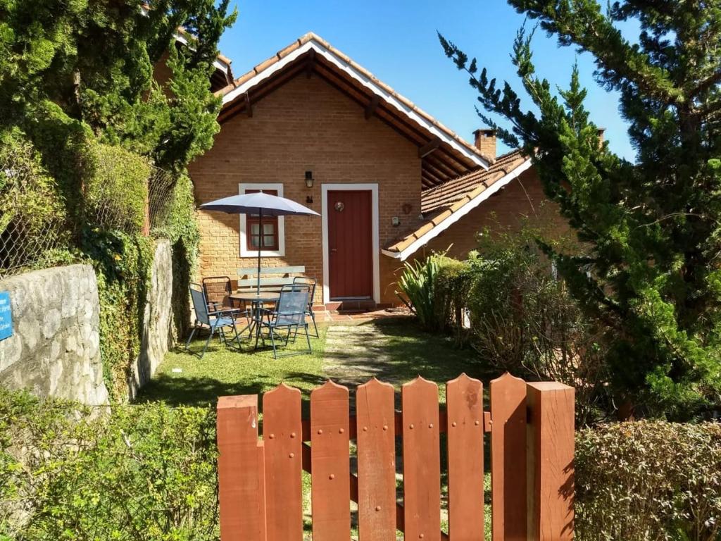 a house with a wooden fence and a table with an umbrella at Chalé dos Alpes I em Monte Verde in Monte Verde