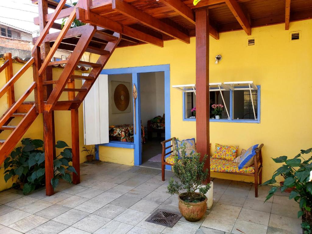 une maison jaune avec un escalier en bois et un banc dans l'établissement Pousada Recanto dos Nativo, à Parati