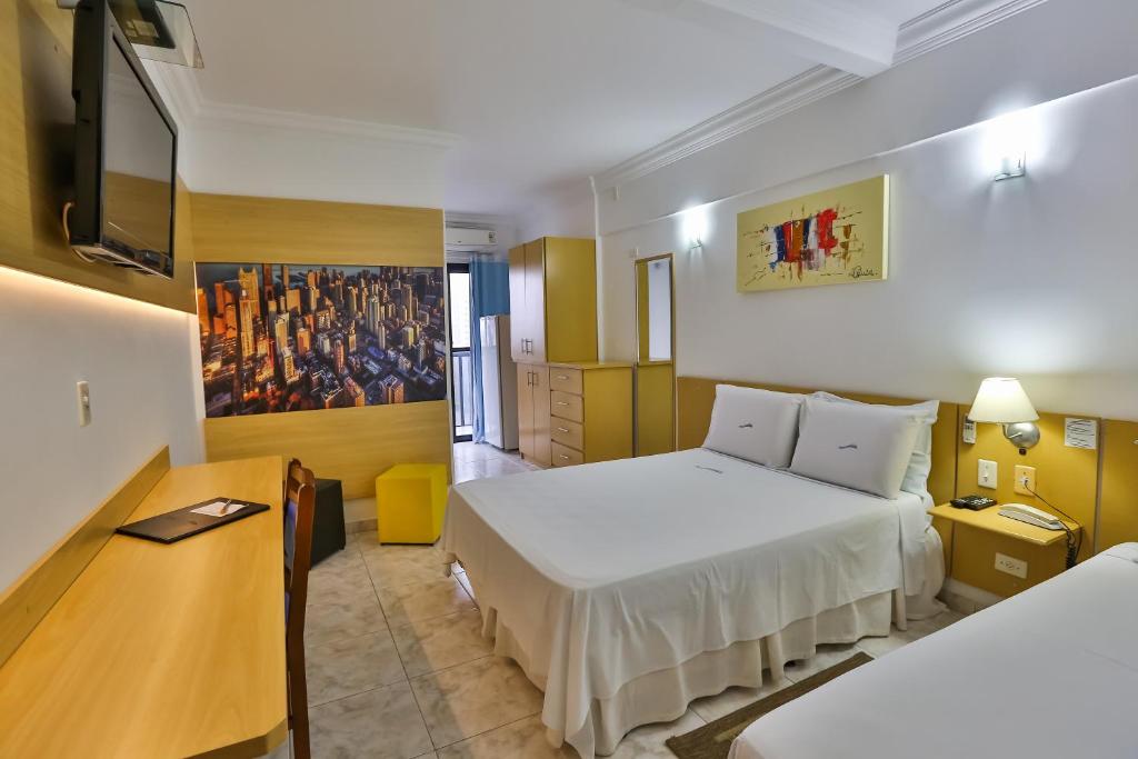 a hotel room with two beds and a desk at HOTEL ROTA DO SOL in Praia Grande